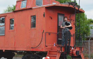 GaN employee playing a bagpipe while standing on a train caboose