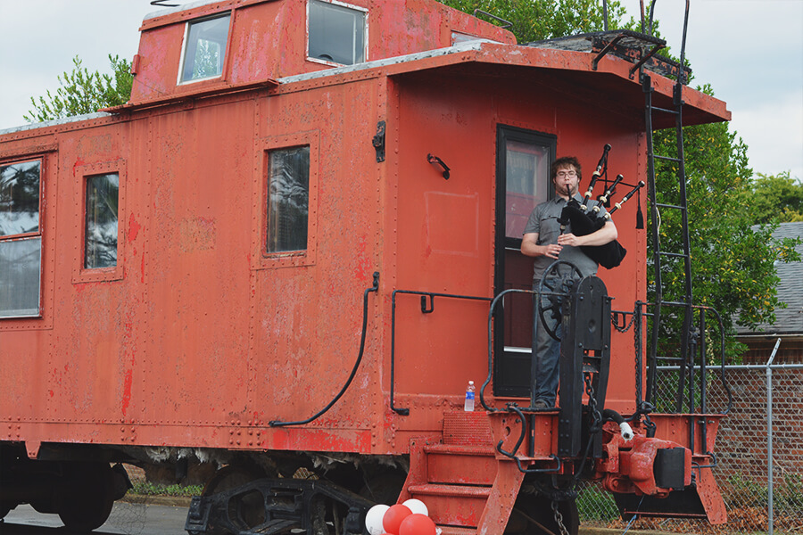 GaN employee playing a bagpipe while standing on a train caboose